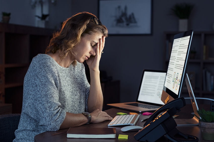 Mature and tired businesswoman working in the office until night. Portrait of a casual stressed lady with headache at desk near desktop computer. Exhausted business woman working late night at computer in office.